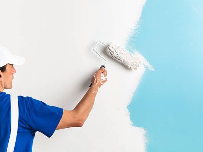 Back view of painter painting a wall with paint roller, with copy space