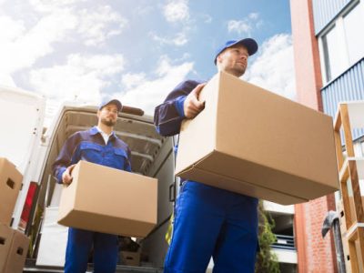 Close-up Of Two Young Delivery Men Carrying Cardboard Box In Front Of Truck